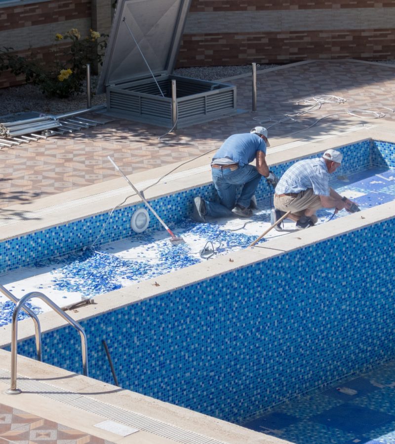 Preparing for the summer season. Two workers repairing a swimming pool in the courtyard of a residential building - Mahmutlar, Alanya, Turkey - May 18, 2021